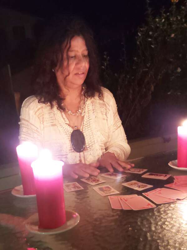 Femme aux cheveux bruns lisant des cartes de tarot roses, éclairée par deux grandes bougies rouges, assise à une table en verre la nuit.