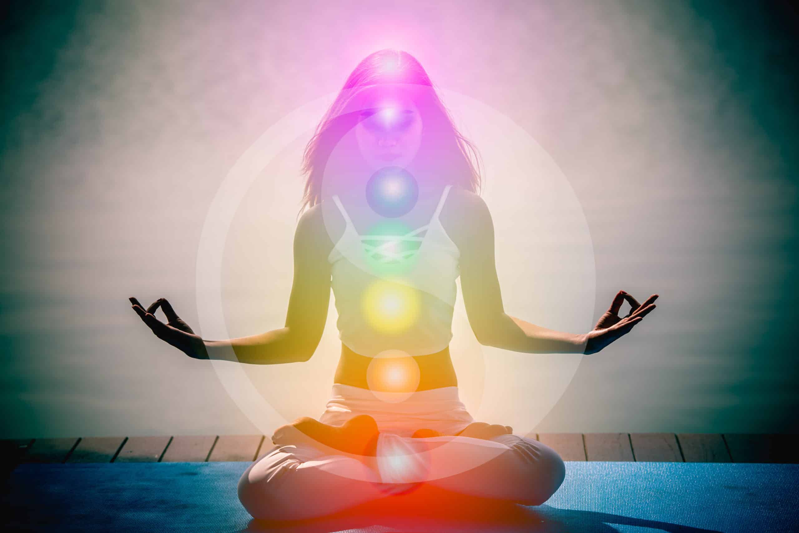 Jeune femme en méditation lotus, mudra de la main, chakras lumineux colorés superposés au corps.