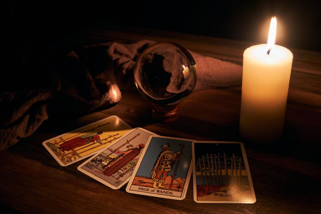 Tirage de tarot mystique sur table en bois sombre : Page of Wands, 7 de Coupes, 8 de Coupes, 10 d'Épées, éclairés par une bougie.