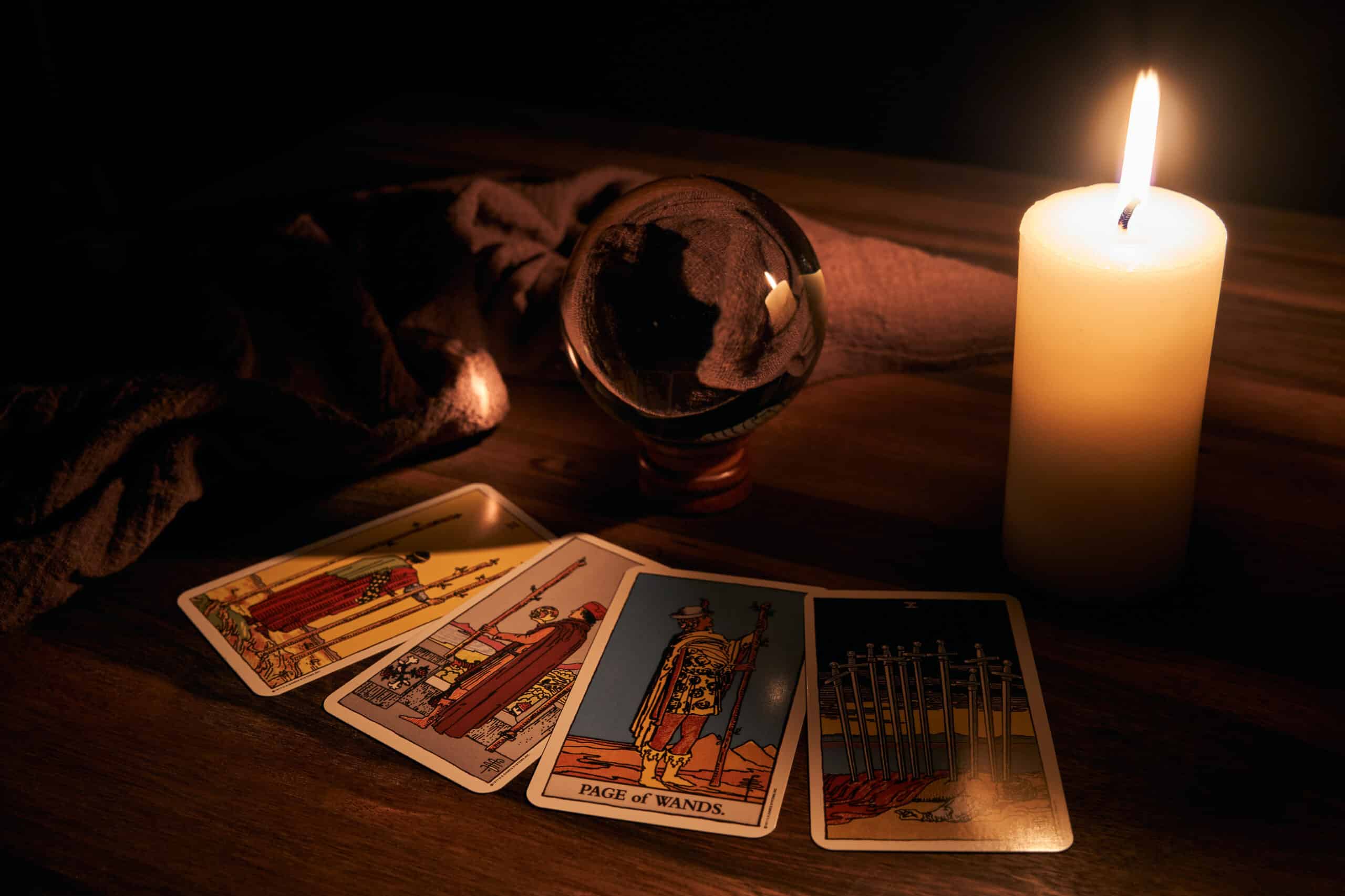 Tirage de tarot mystique sur table en bois sombre : Page of Wands, 7 de Coupes, 8 de Coupes, 10 d'Épées, éclairés par une bougie.